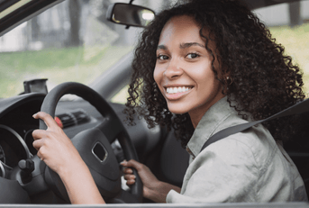 A young woman smiles while driving her car and wearing her seatbelt.