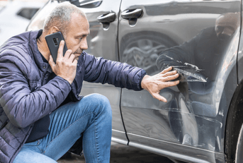 A man runs his hands over a dent in his car's rear door panel.