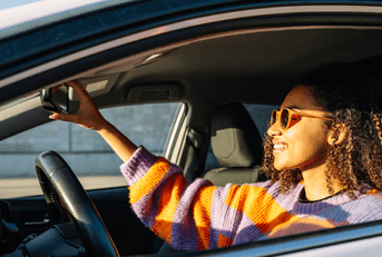 A woman in a striped sweater adjusts her rearview mirror in her car.