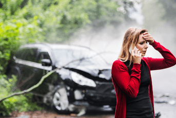 A woman clutches her head and calls someone on the phone after getting into a car accident.
