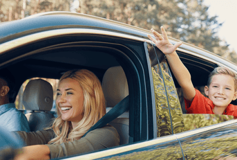 A little boy sticks his hands out of the window as his mom drives the car.
