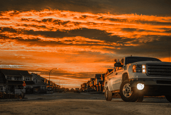 A white GMC Sierra is shown with its headlights on against an orange sky.