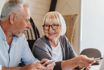 wife and husband sit on couch using computer