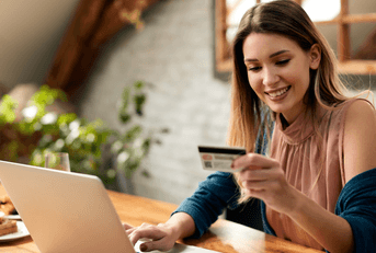 A woman smiles while holding a credit card and using her laptop in her home office.