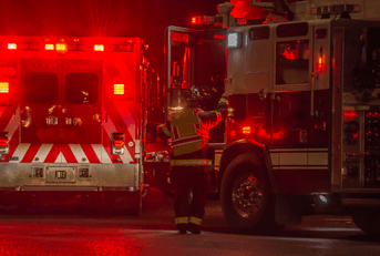 A firefighter walks toward the fire truck with an ambulance in the background.
