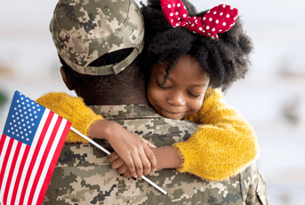 A little girl holds an American Flag while giving her military family member a hug.