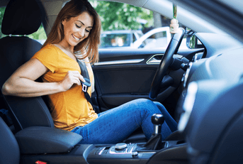 A woman in an orange shirt smiles as she puts on her seatbelt.
