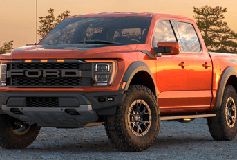 A new orange Ford F-150 Raptor is shown in a parking lot.