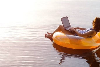 Woman working on a laptop in an inflatable ring in the pool