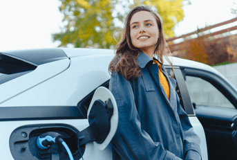 A woman leans against her electric car while it's being charged.