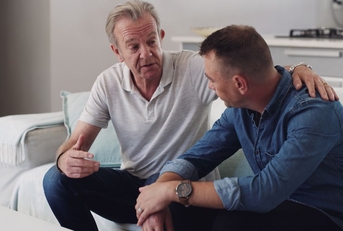 Older father sitting on couch having a serious conversation with his adult son
