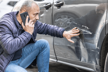 Man looking at car with dent