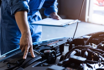 mechanic with a clipboard checking a car engine