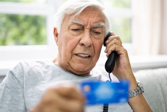 senior man calling while holding credit card