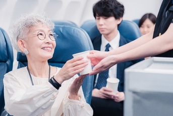 Asian older woman getting served drink in flight