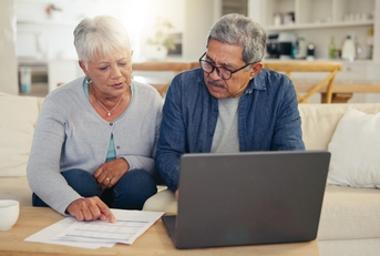 elderly couple using laptop with documents