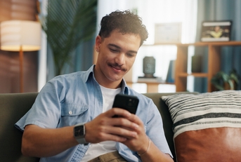 Man playing on phone sitting on couch while smiling slightly
