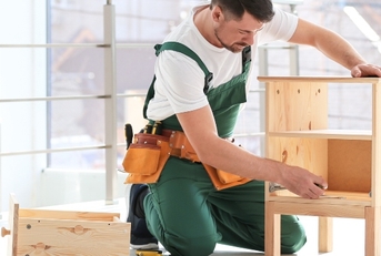 Handyperson wearing overalls assembling wooden furniture