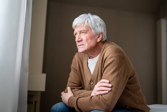Senior man sits staring blankly out window