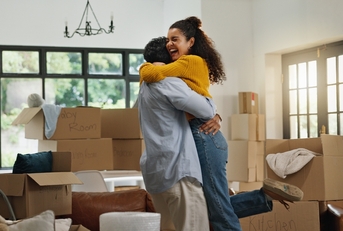 Young couple hugging and celebrating with boxes stacked around them in new house