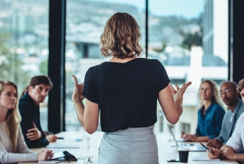 Business woman standing with its back to camera speaking to table of people