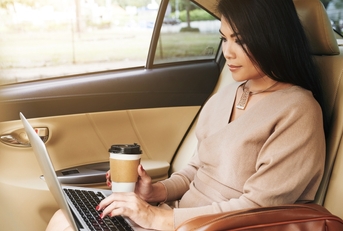 Woman using laptop computer in car while holding a to-go coffee cup