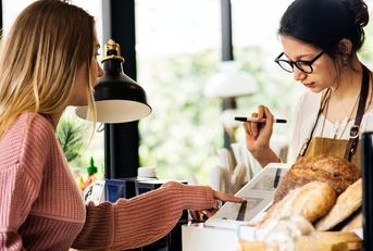 Woman paying on tablet at the bakery with register employee watching
