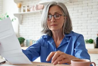 senior mature business woman holding paper bill using calculator managing account finance while sitting at home kitchen table