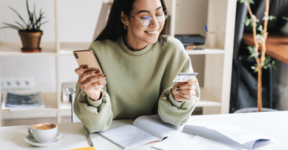 A woman smiles as she holds her phone and a credit card. 