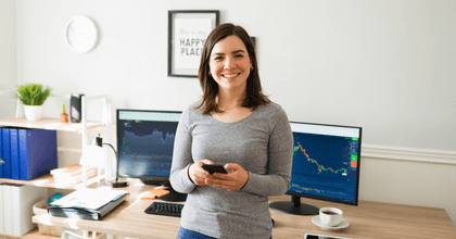 A woman holds her phone while smiling in front of computers.