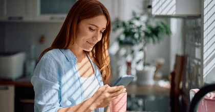 Smiling woman looking at her phone and holding a mug