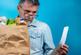 man looking at receipt in hand while holding brown grocery bag