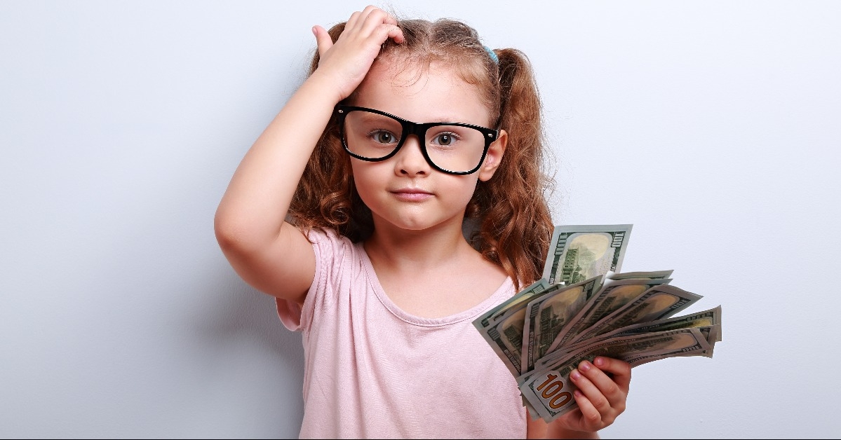 Small girl in eye glasses scratching head, holding money
