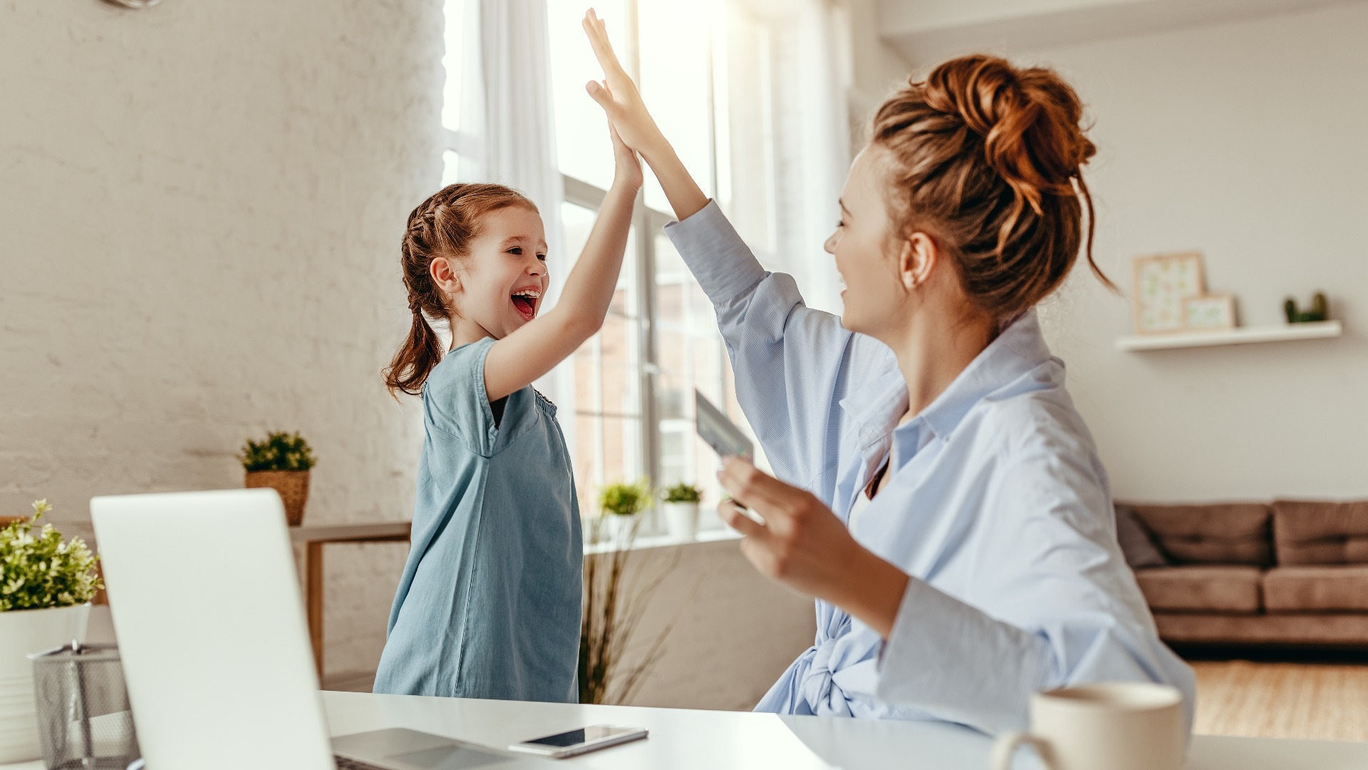Happy woman giving high five to small girl after successful purchase on Internet using computer at home