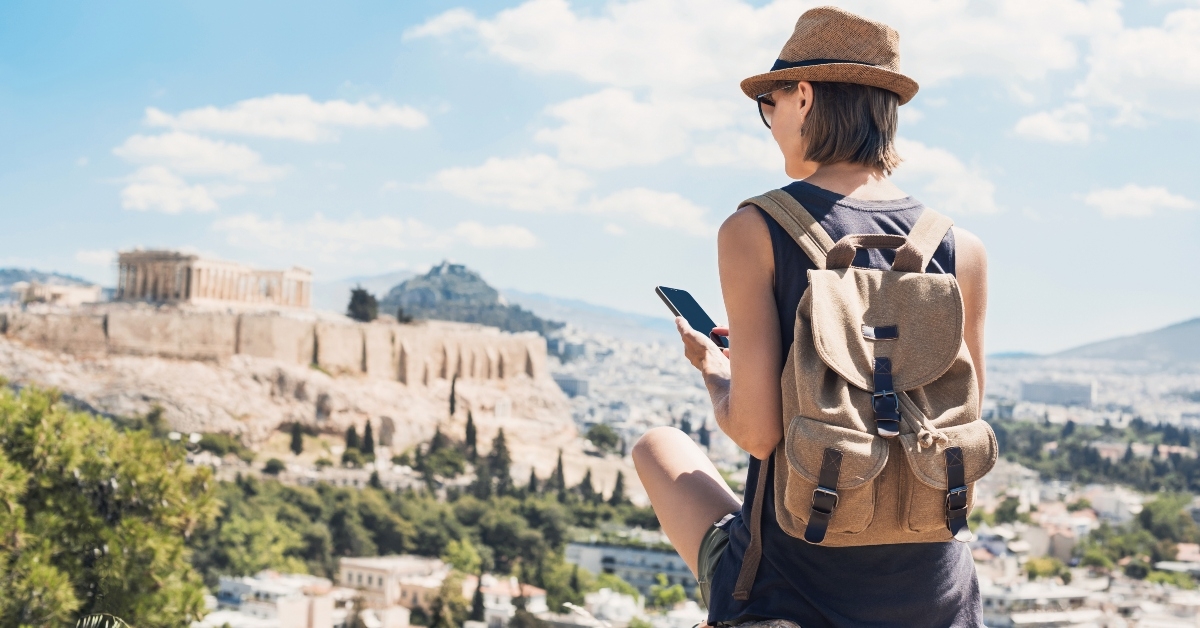 Woman in Greece with backpack and hat looking at phone