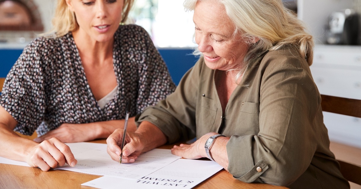 Female Friend Helping Senior Woman To Complete Last Will And Testament At Home