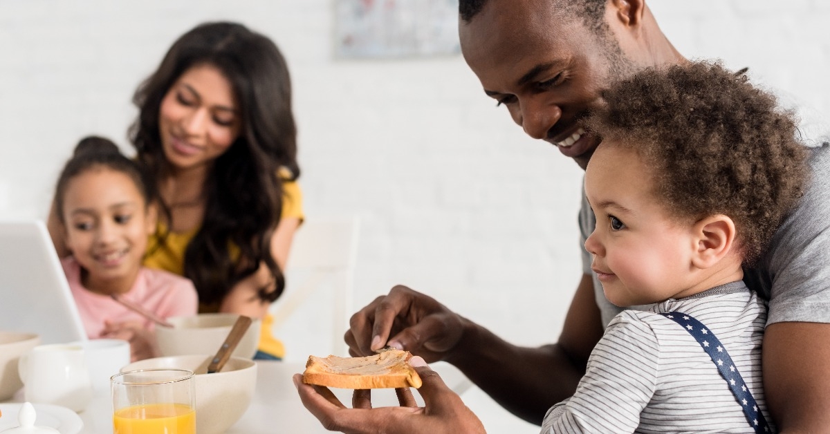 father applying peanut butter on toast for son at kitchen