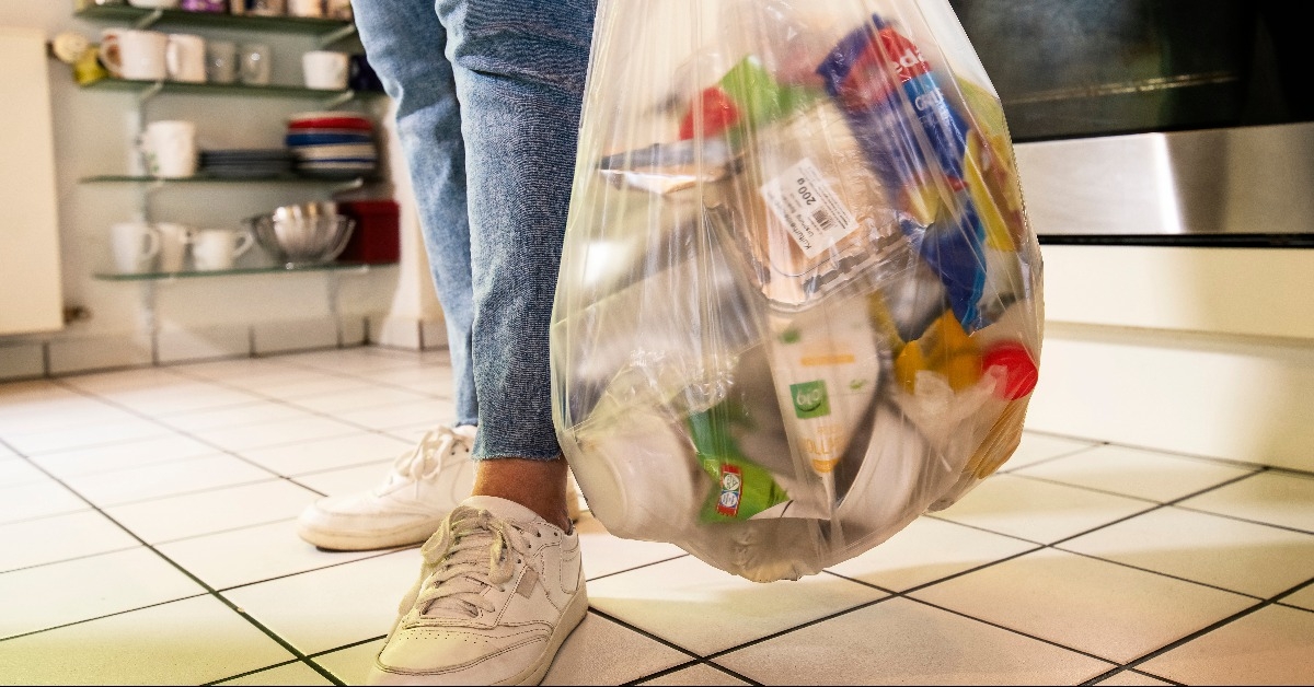 woman standing in a kitchen carrying a bag with plastic waste
