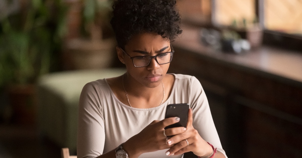 Upset confused African woman holding cellphone having problem with phone