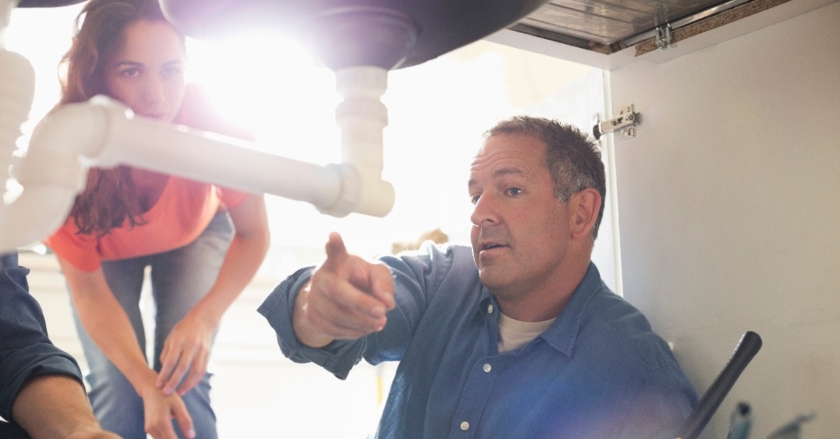 plumber working on pipes under sink
