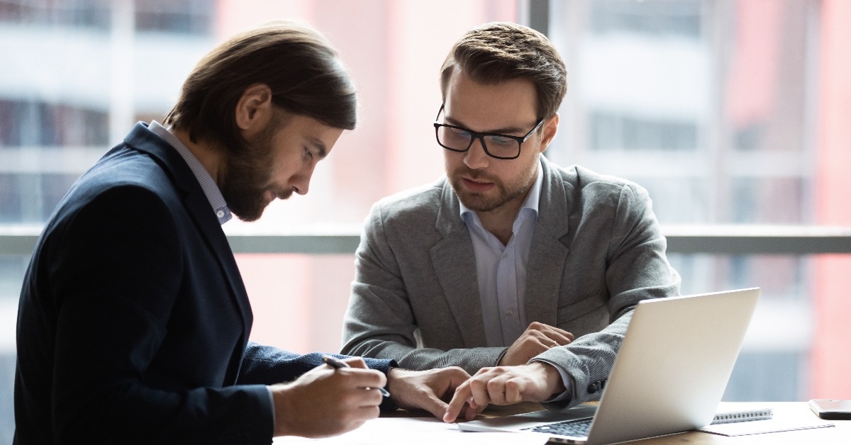 young businessman signing agreement with skilled lawyer in eyeglasses