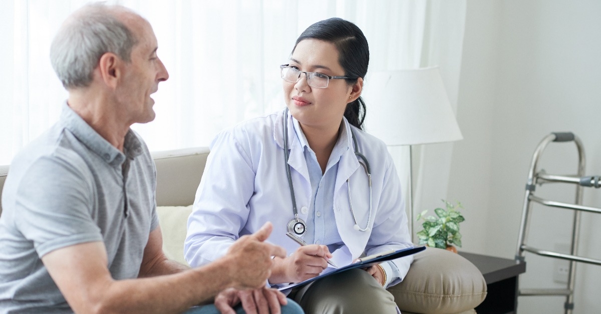 asian adult woman with clipboard sitting on sofa in house of senior man
