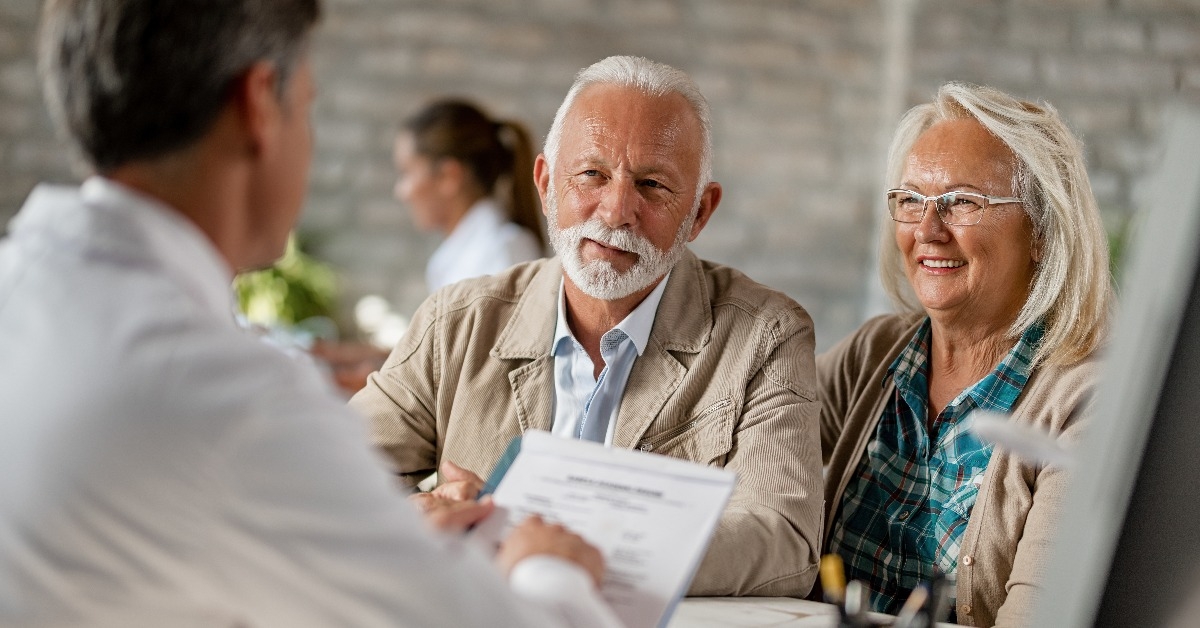 happy senior couple going through medical insurance paperwork with a doctor