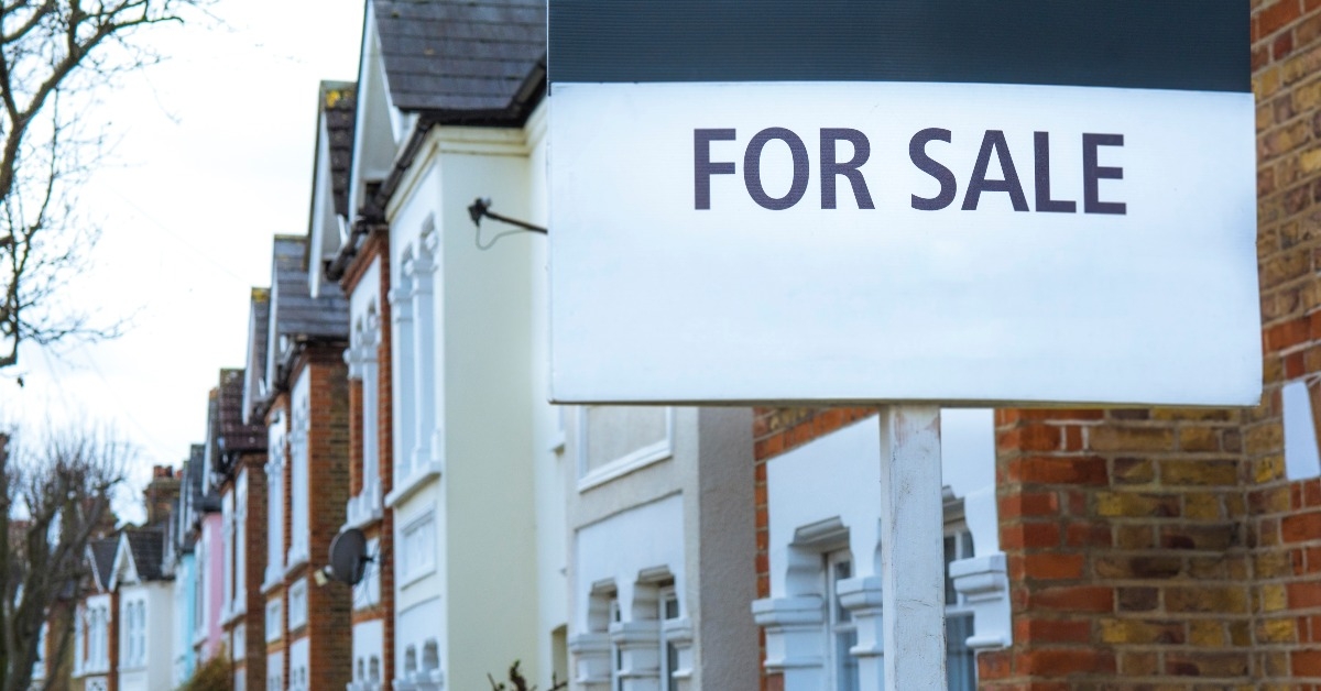 'For Sale' estate agent sign on street of terraced houses