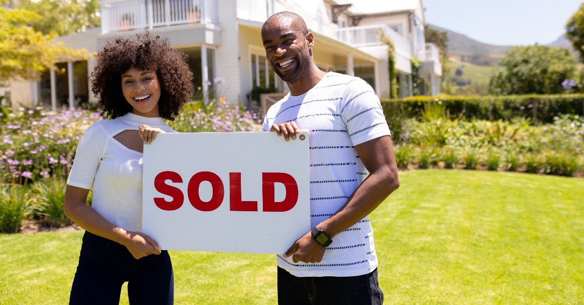 happy young african american couple in the garden holding sold sign