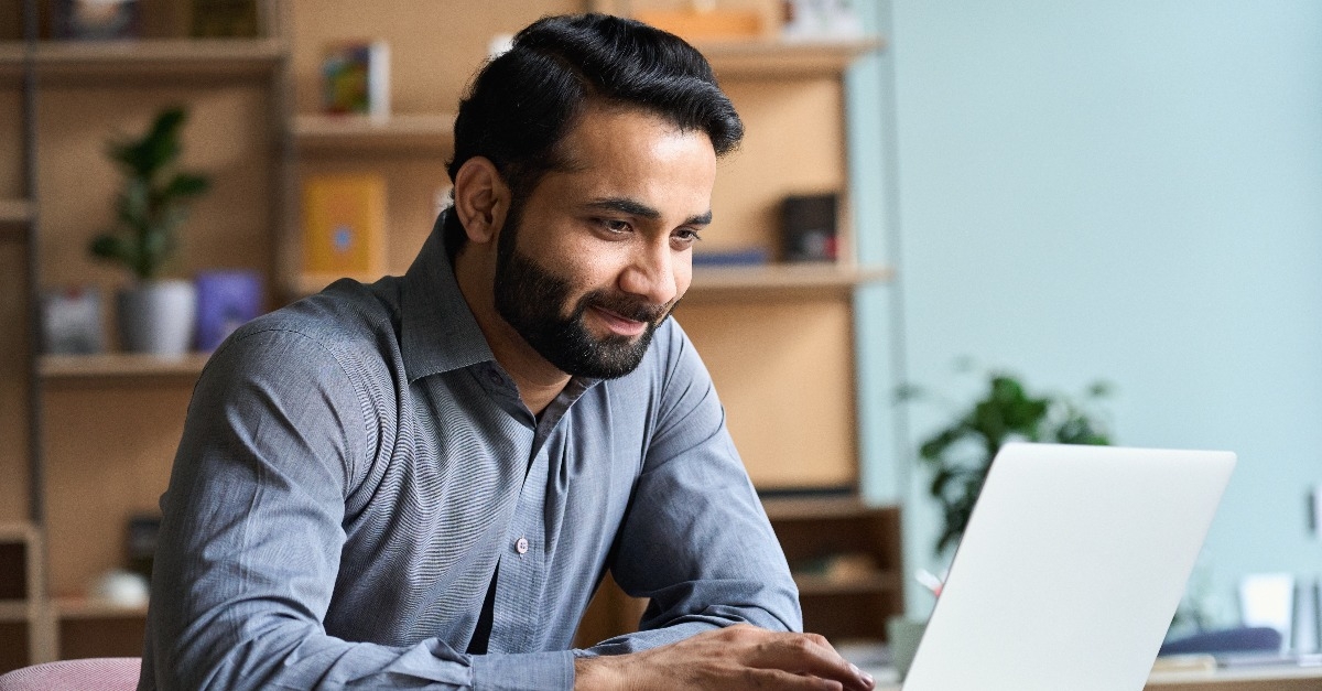 Smiling indian business man working on laptop 