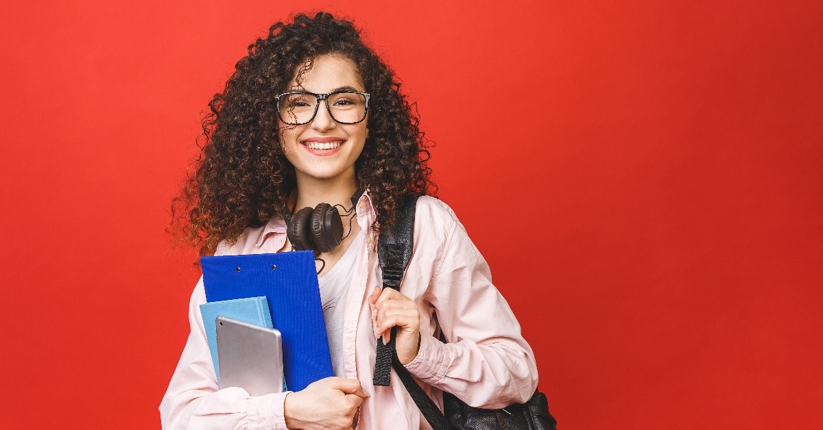 young curly student woman wearing backpack glasses holding books and tablet 