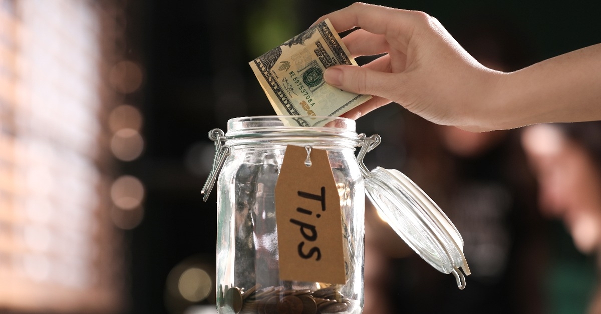 woman putting tips into glass jar on wooden table