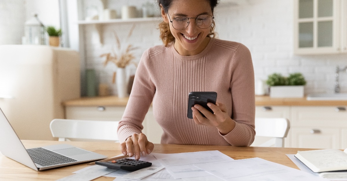 smiling young woman in eyewear looking at smartphone screen