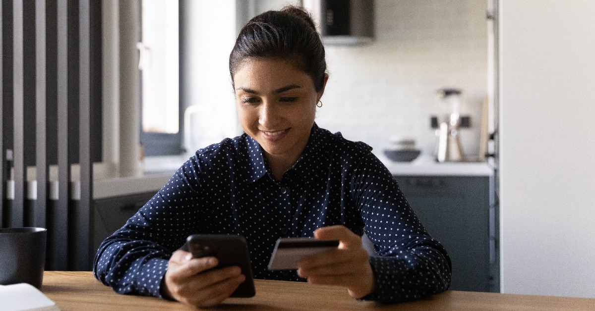 young indian woman sit at home desk holding credit card